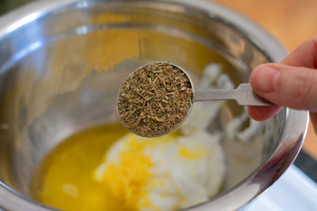 spoon full of Greek seasoning over bowl on ingredients
