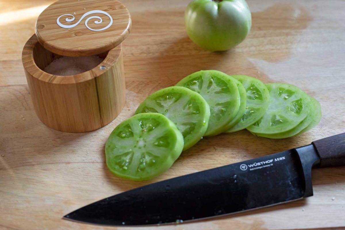 sliced green tomatoes on cutting board with knife and salt