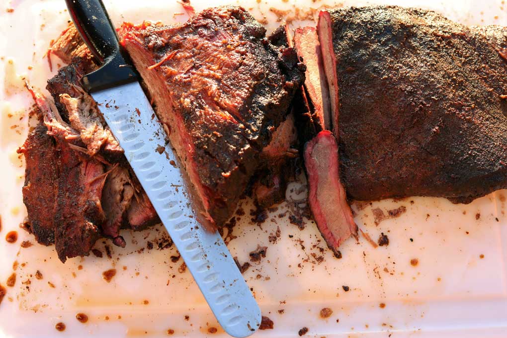 sliced whole smoked brisket on cutting board with knife