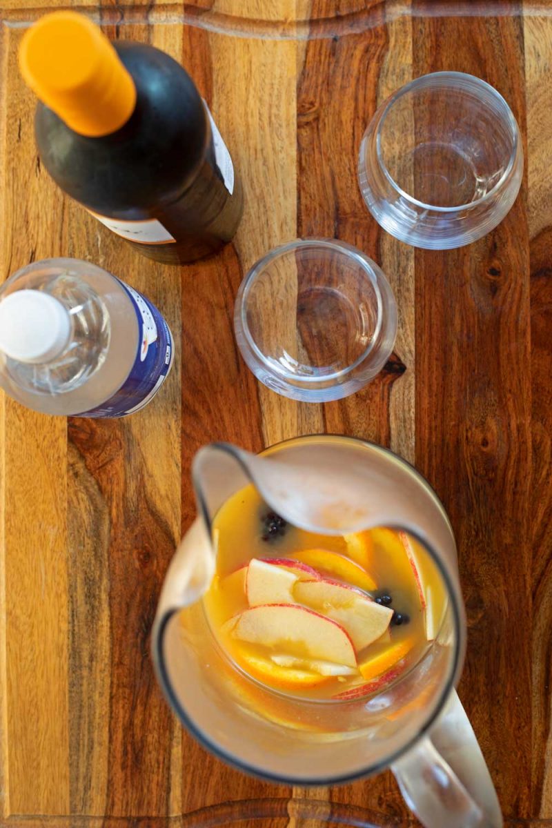 pitcher of fruit and juice with two glasses a bottle of wine and club soda