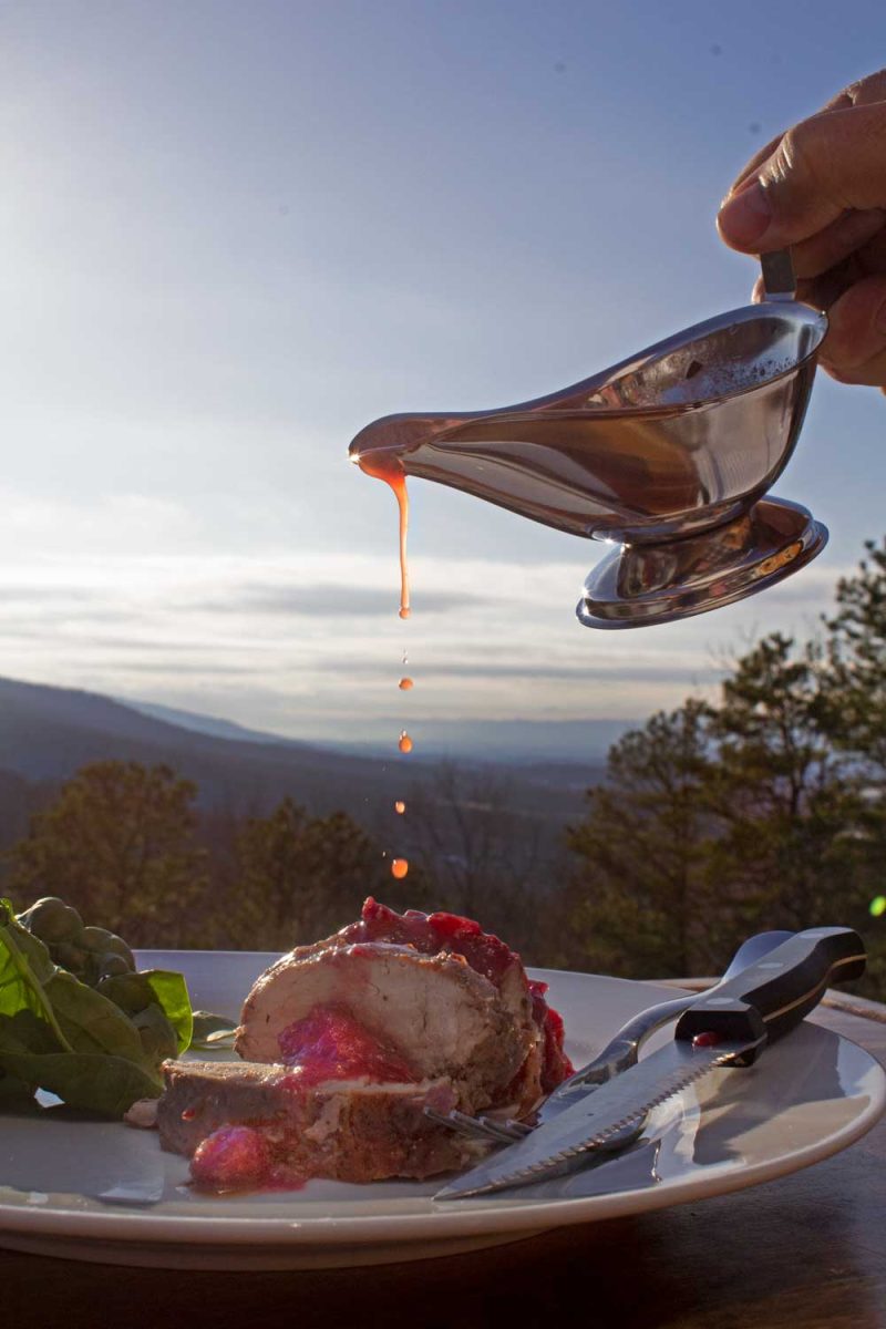 pork tenderloin sliced on plate with gravy boat drizzling cranberry sauce