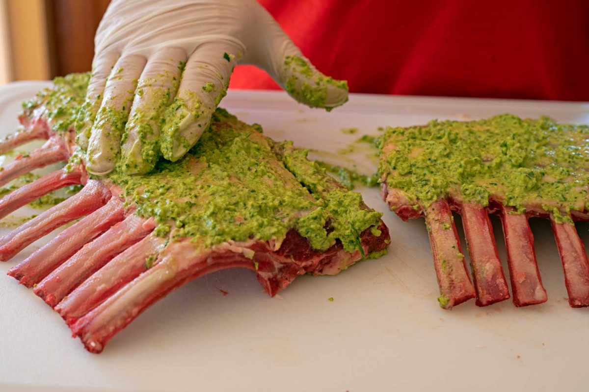 hand smearing fresh herb wet rub over lamb