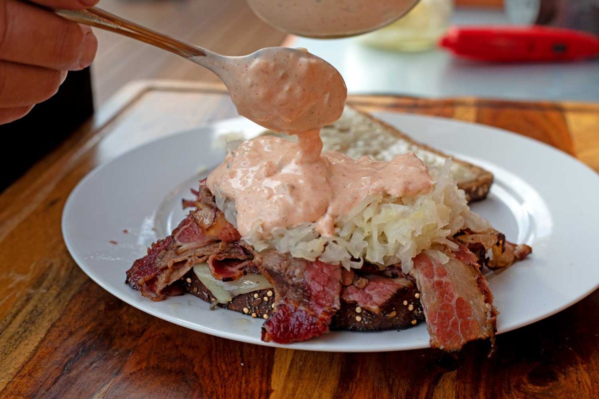 spoon pouring Thousand Island dressing over Reuben