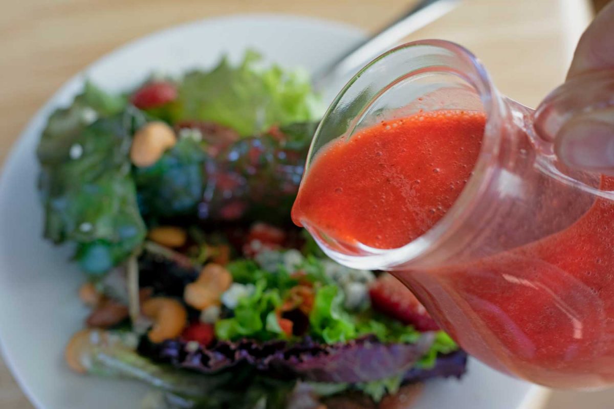 pouring strawberry vinaigrette onto spring mixed berry salad