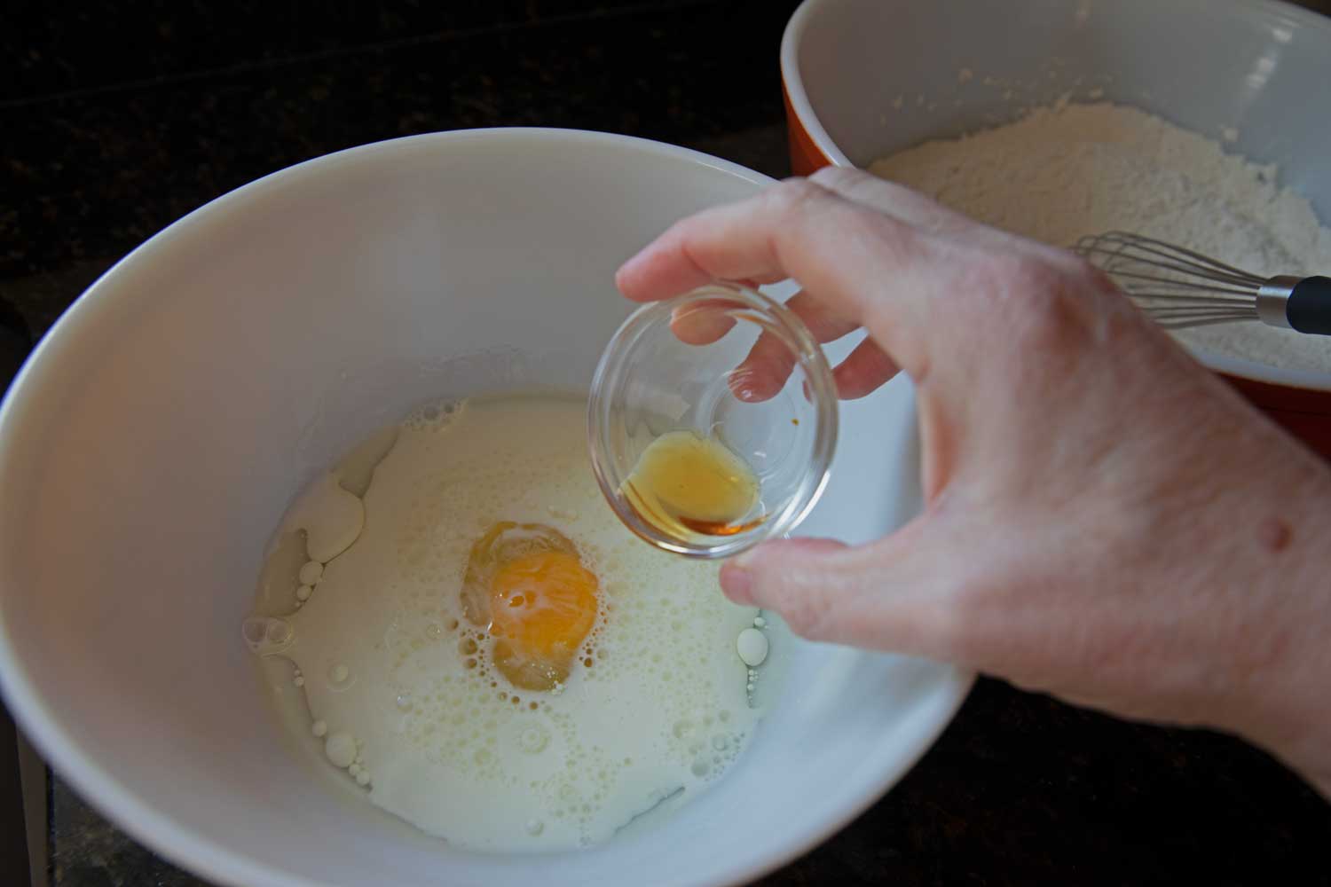 pouring vanilla into bowl of milk, oil and egg
