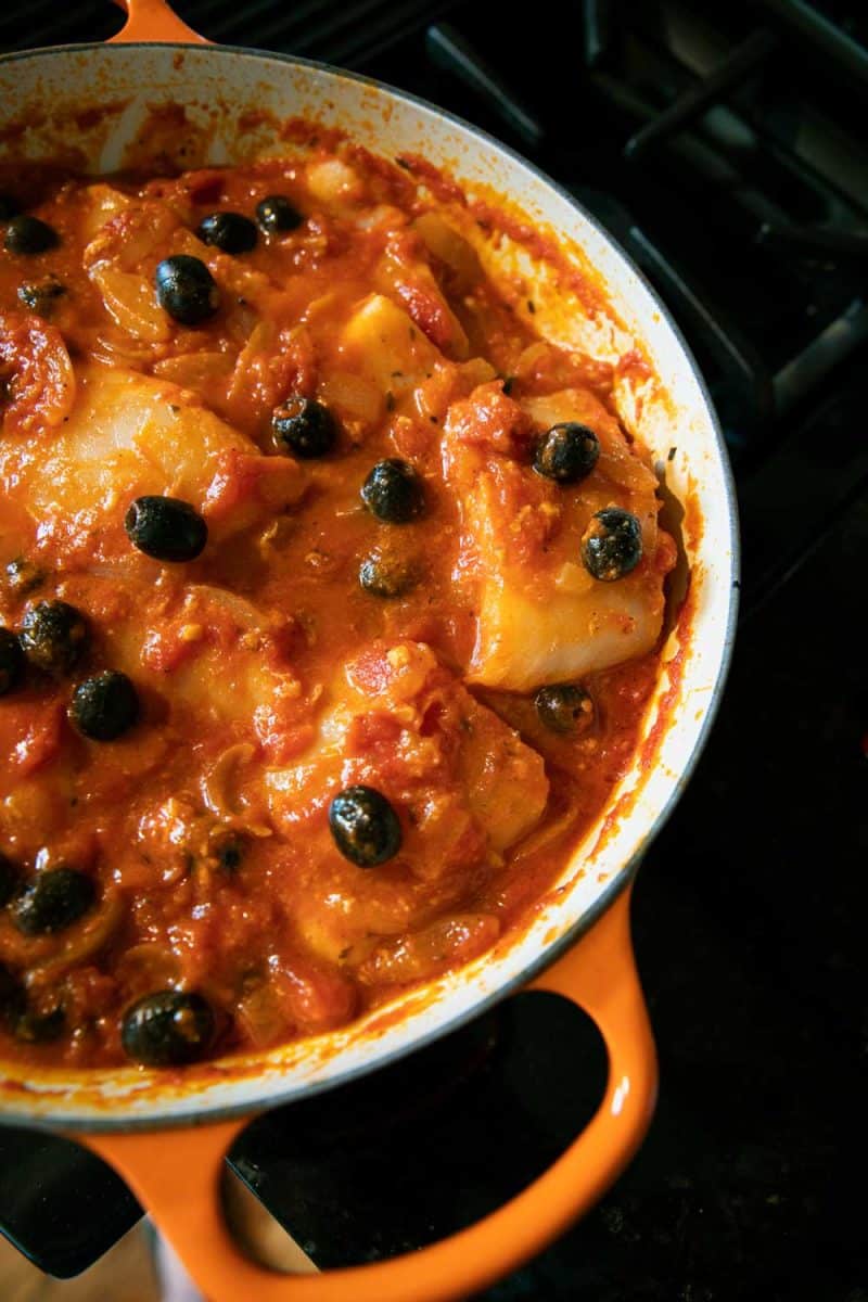 poached fish with tomatoes and olives in skillet