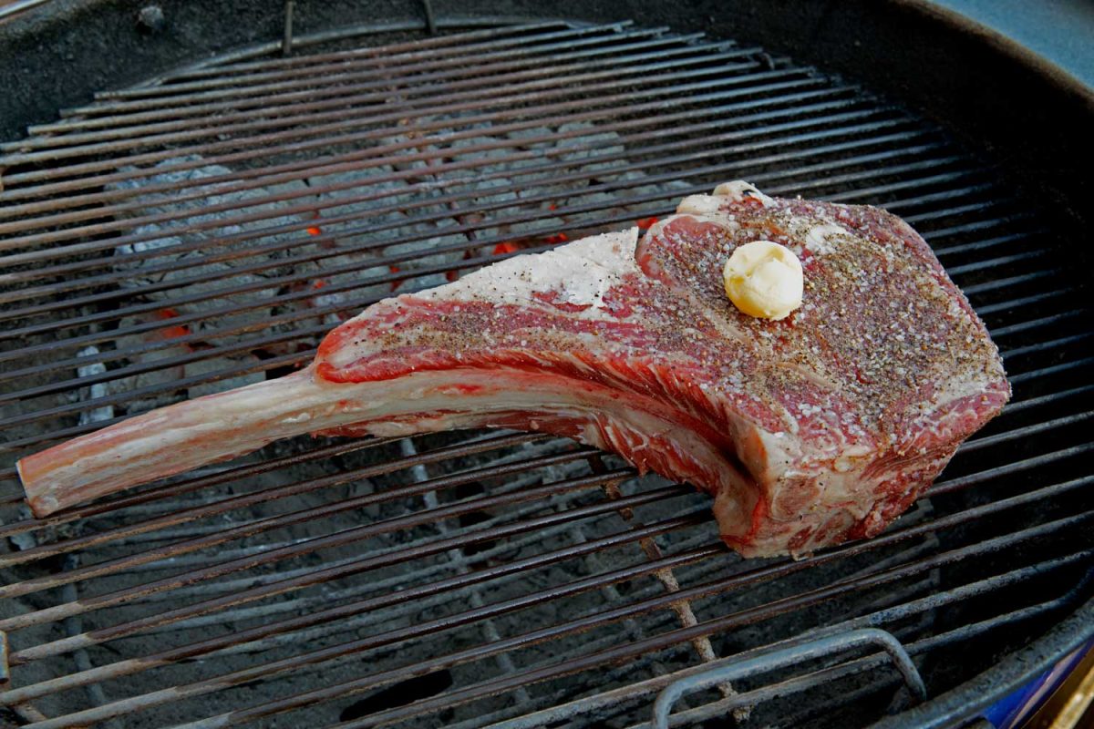 raw steak on grill with pat of butter