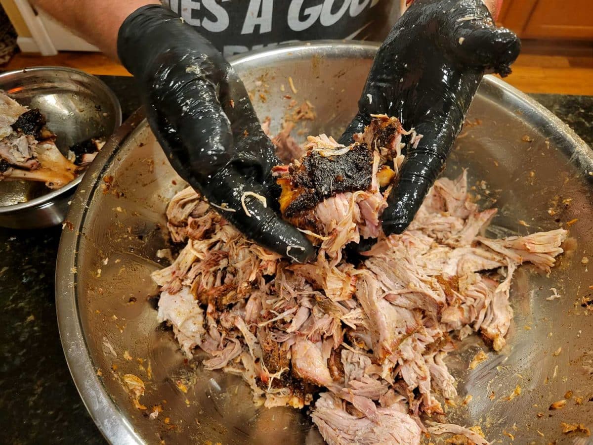gloved hands with pulled pork in a bowl