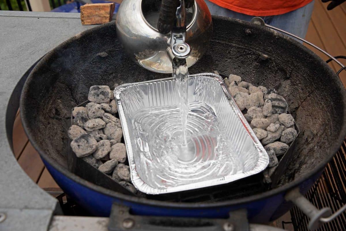 pouring water into disposable aluminum pan in bottom of grill