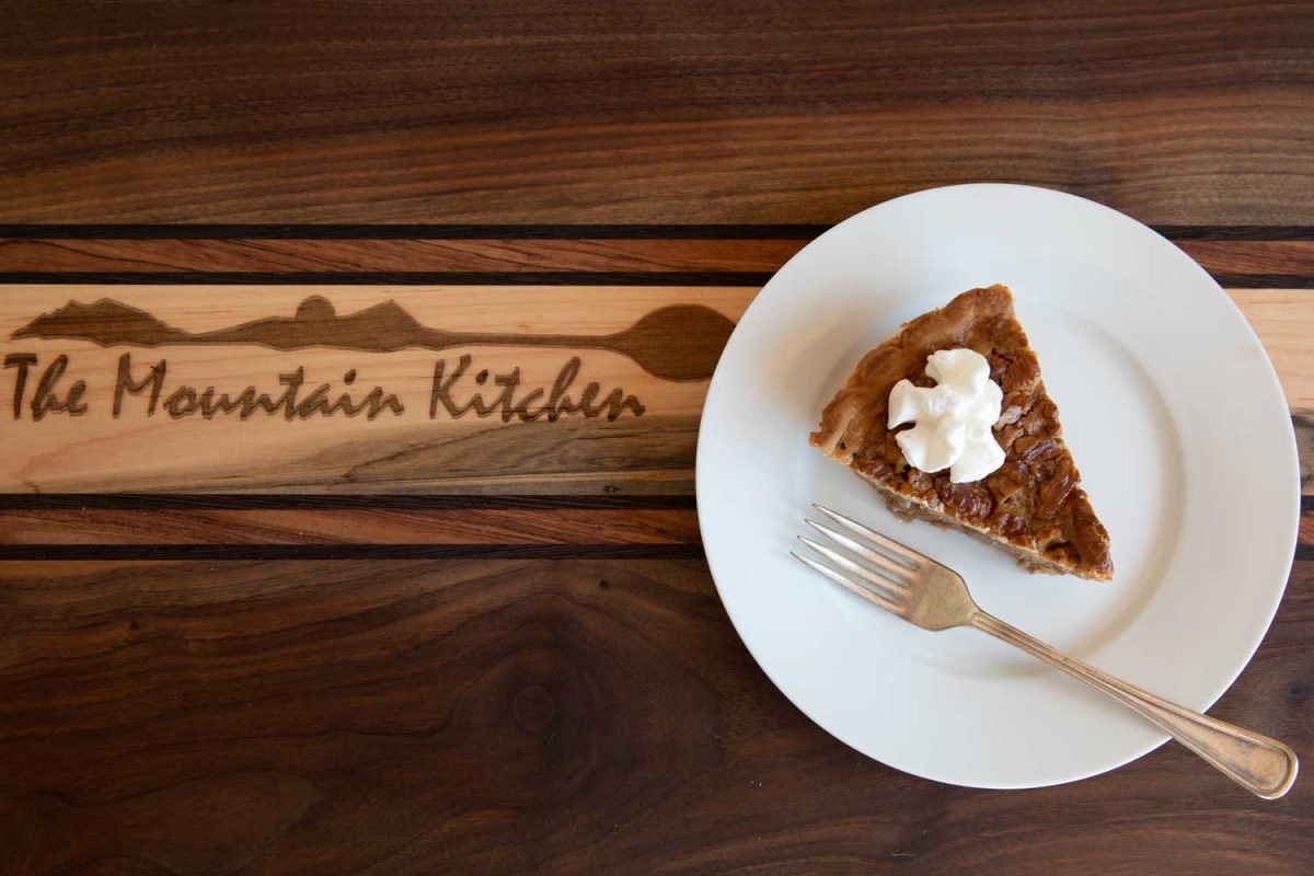 slice of pecan pie on cutting board with whipped cream on top