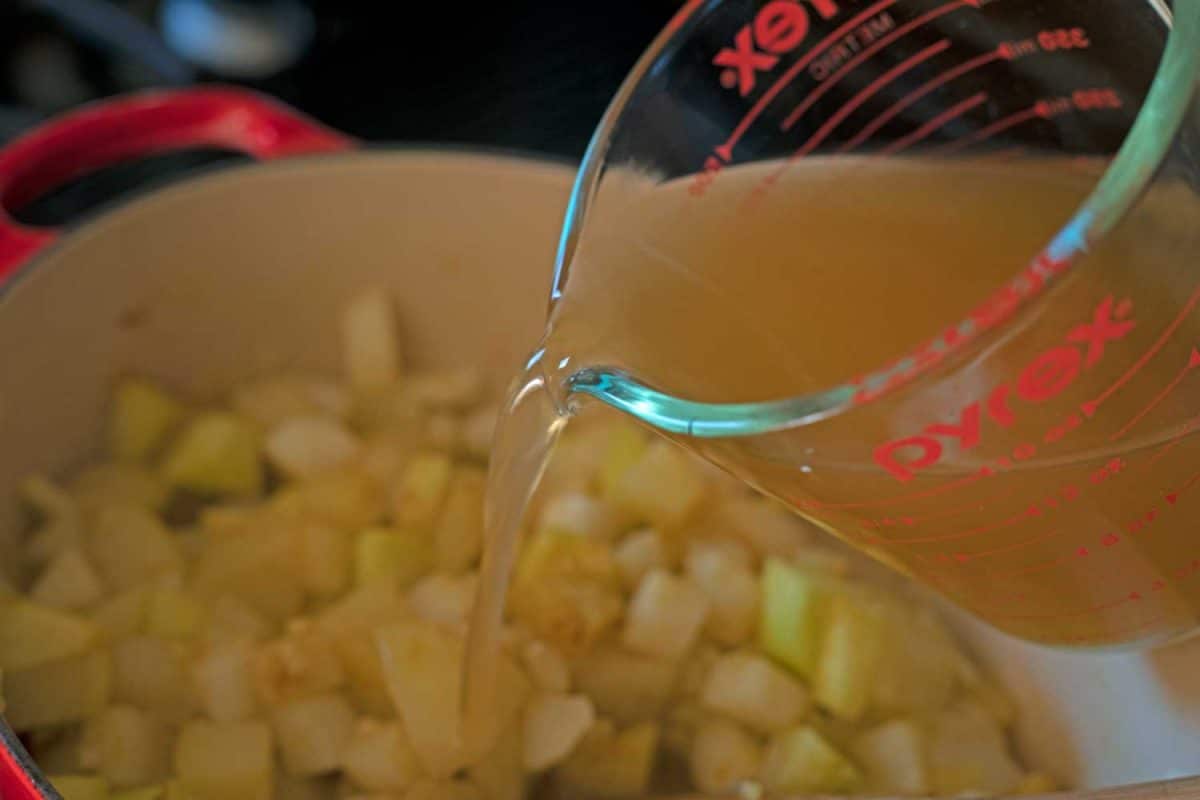 pouring broth into pot of soup