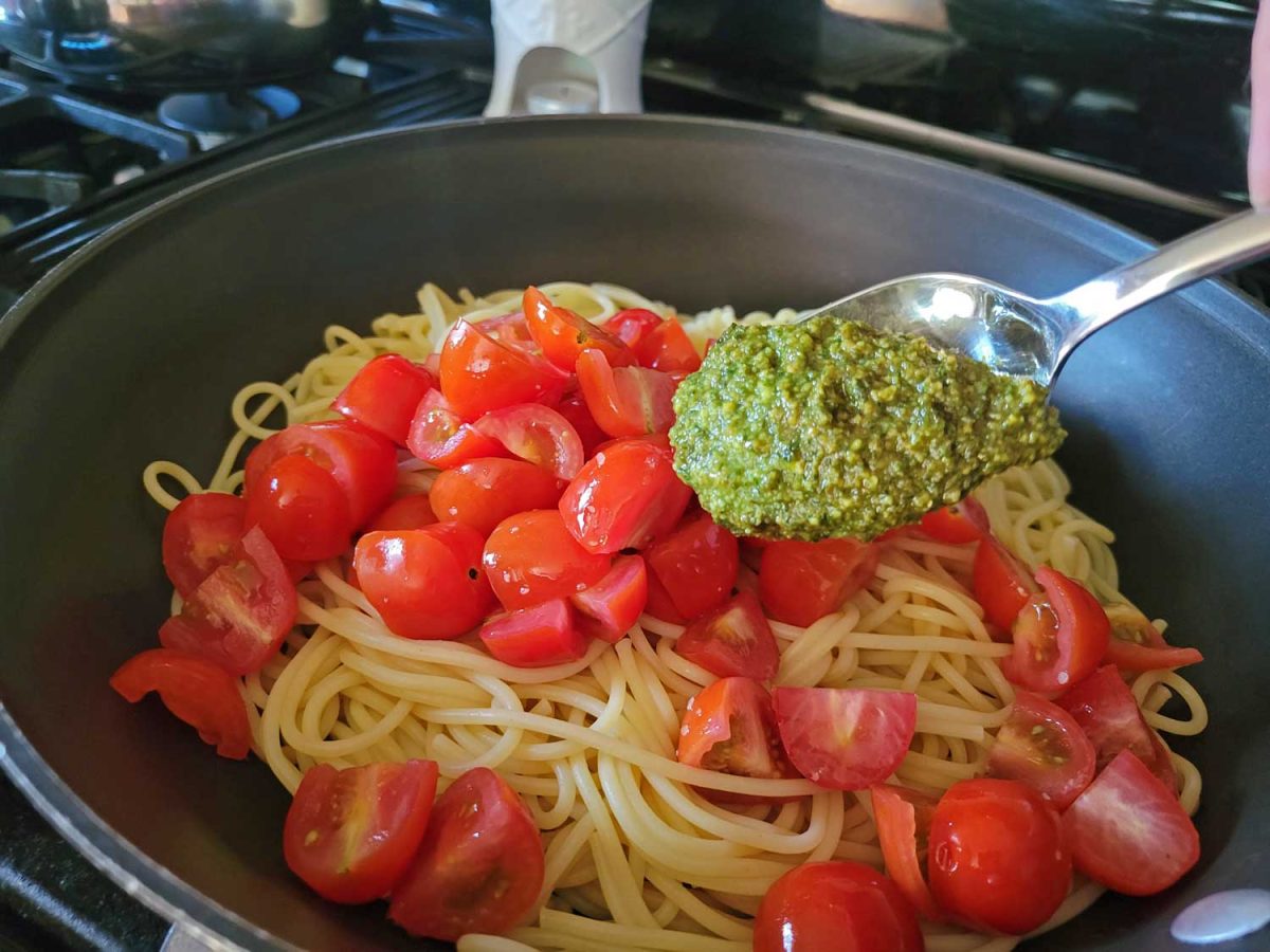 adding pesto to pasta with tomatoes