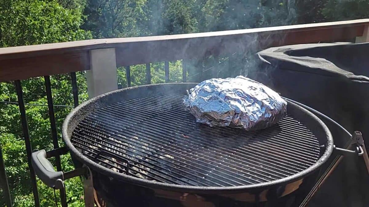 pork butt wrapped in aluminum foil on grill