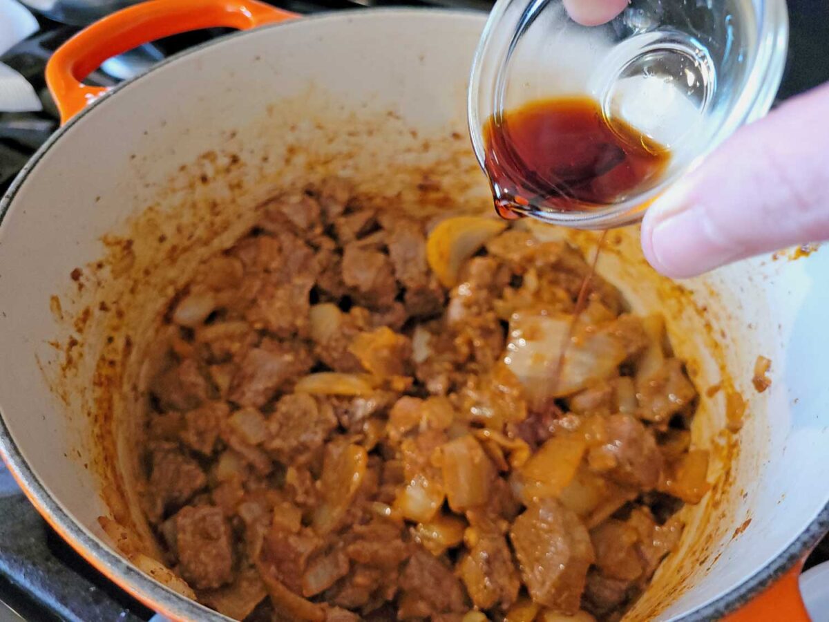 pouring soy sauce into the pot of stew